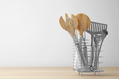 Set of kitchen utensils in stand on wooden table near light wall. Space for text