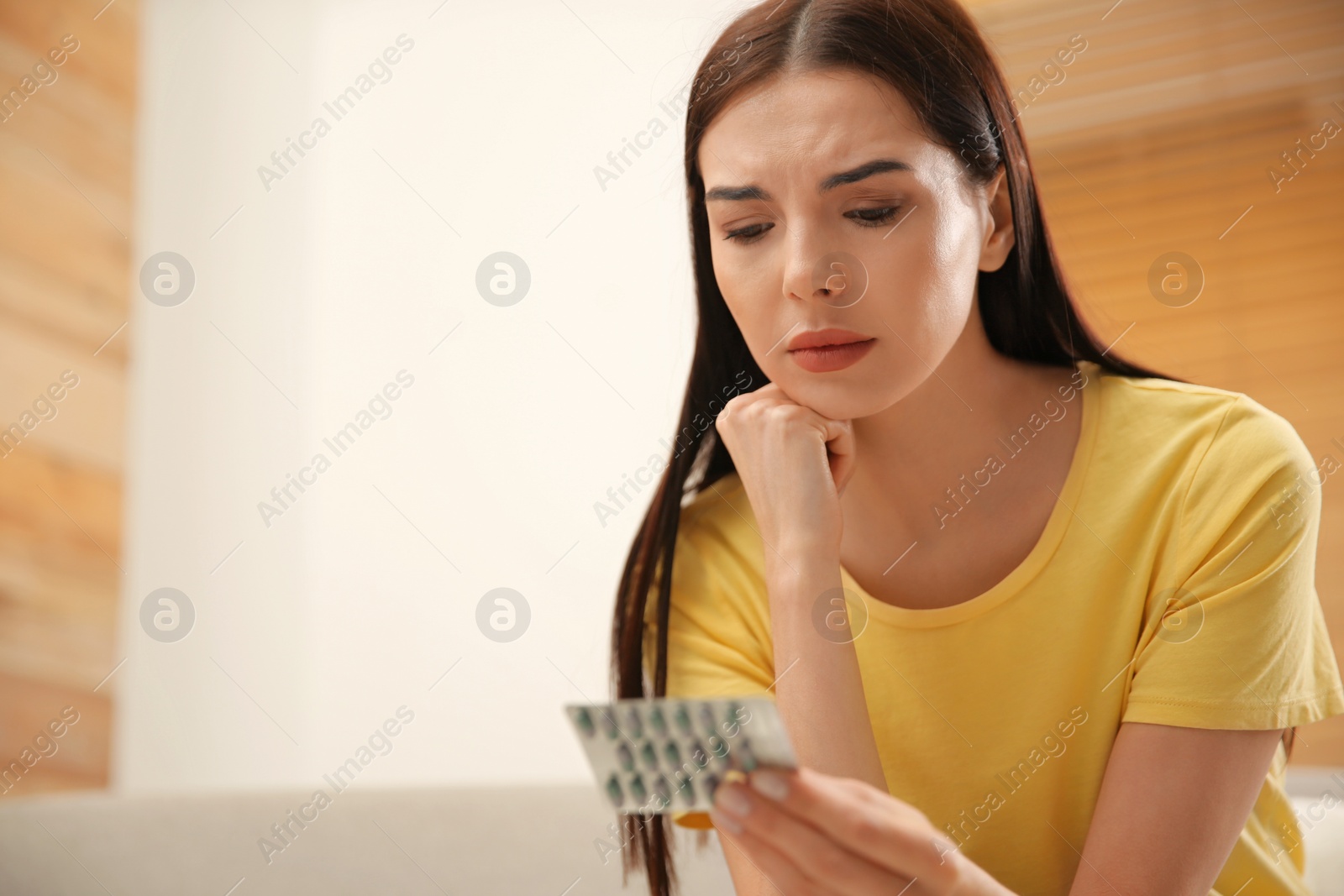 Photo of Confused young woman holding package of pills at home. Space for text