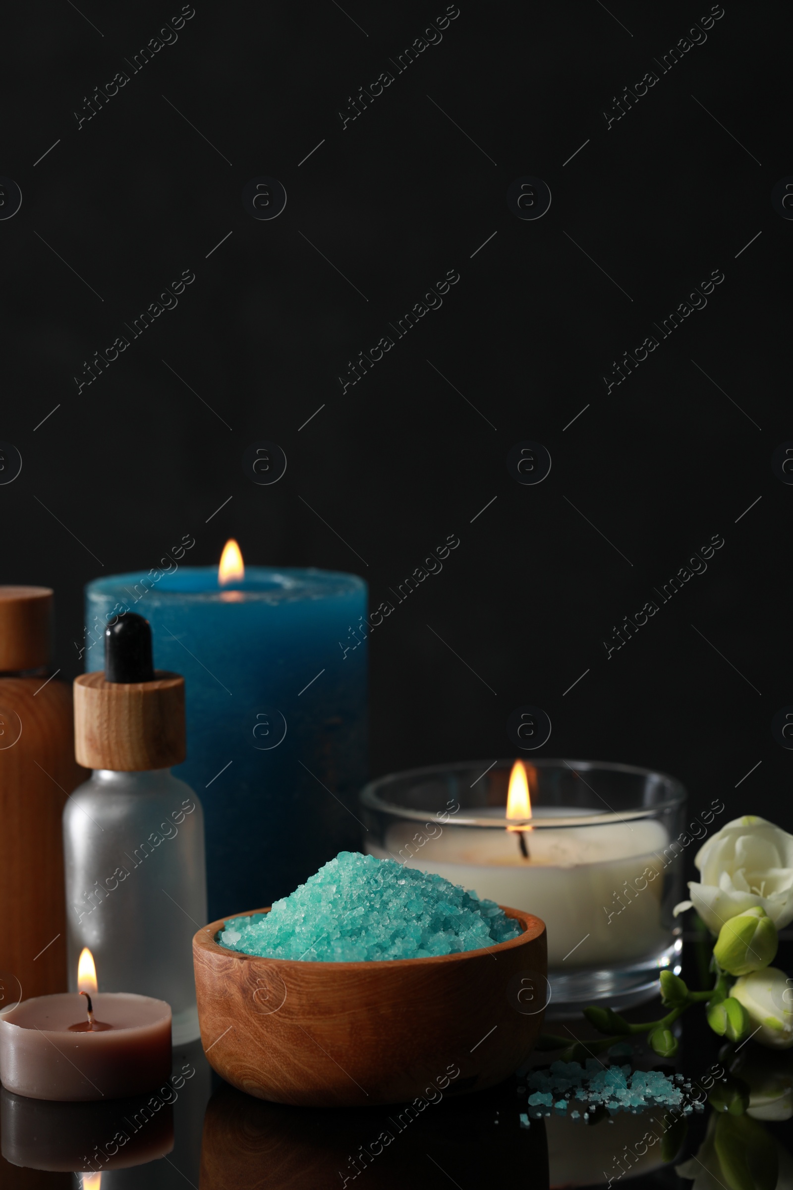 Photo of Beautiful spa composition with different care products, burning candles and flowers on black mirror surface