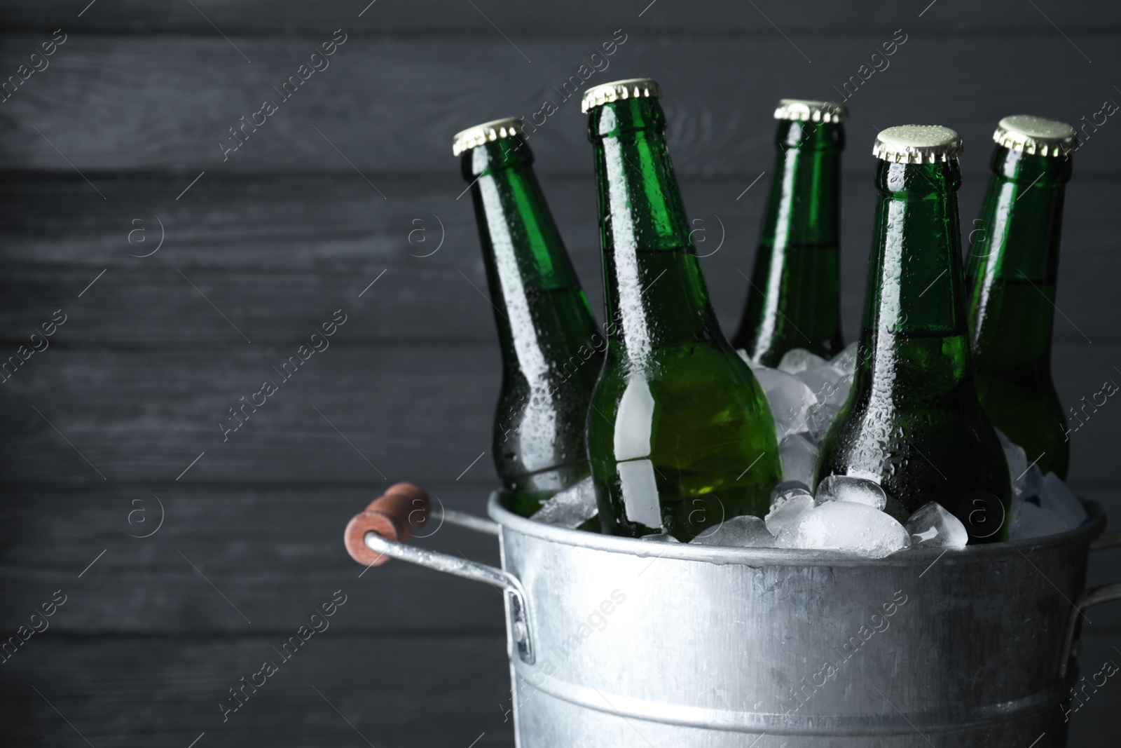 Photo of Metal bucket with bottles of beer and ice cubes on dark wooden background, closeup. Space for text