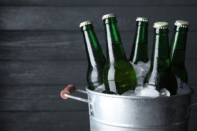 Photo of Metal bucket with bottles of beer and ice cubes on dark wooden background, closeup. Space for text