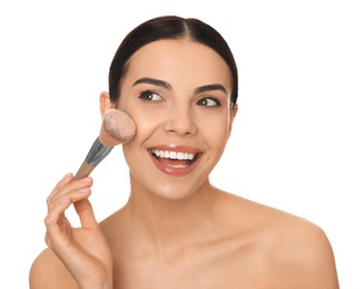 Beautiful young woman applying face powder with brush on white background