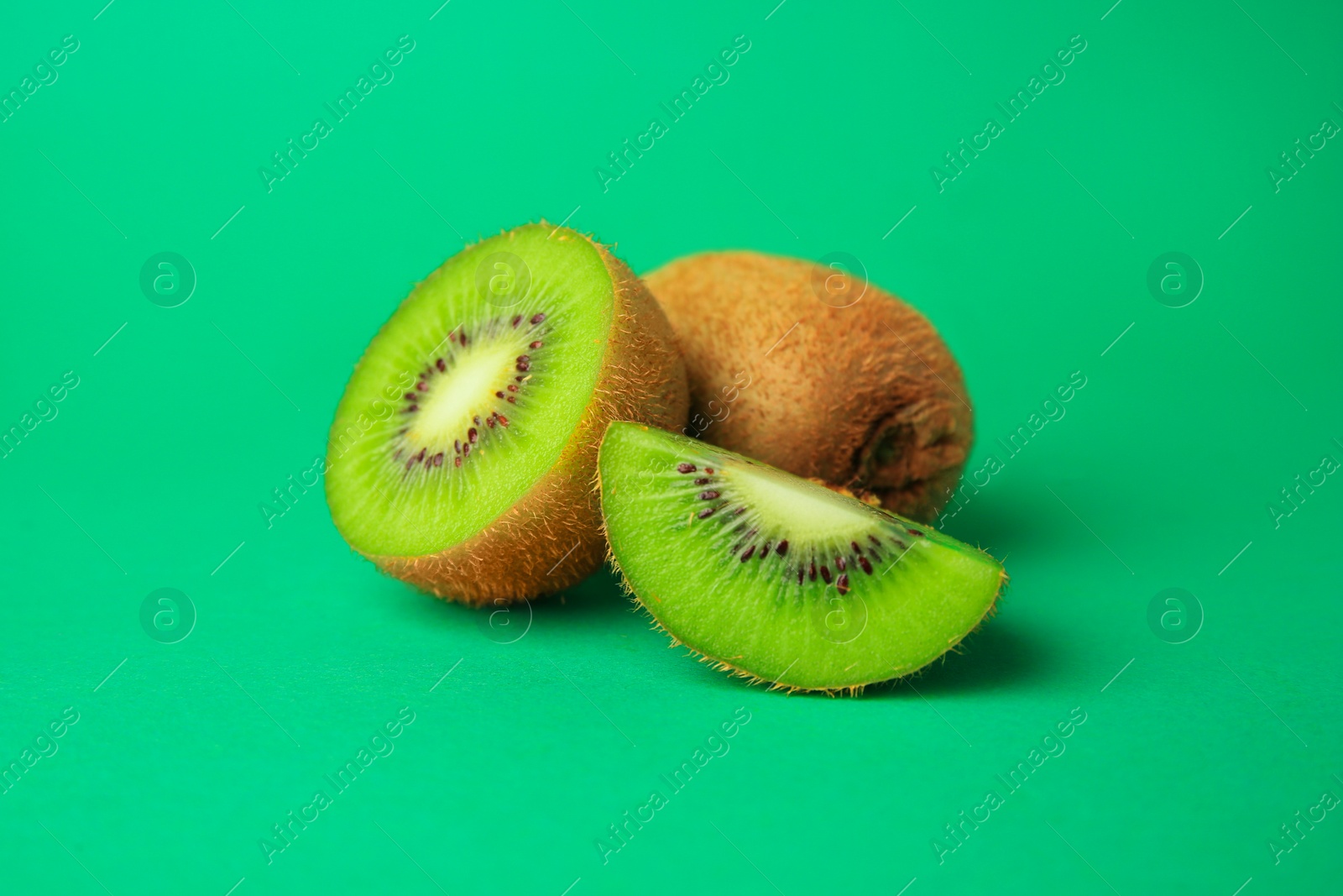 Photo of Whole and cut fresh kiwis on green background