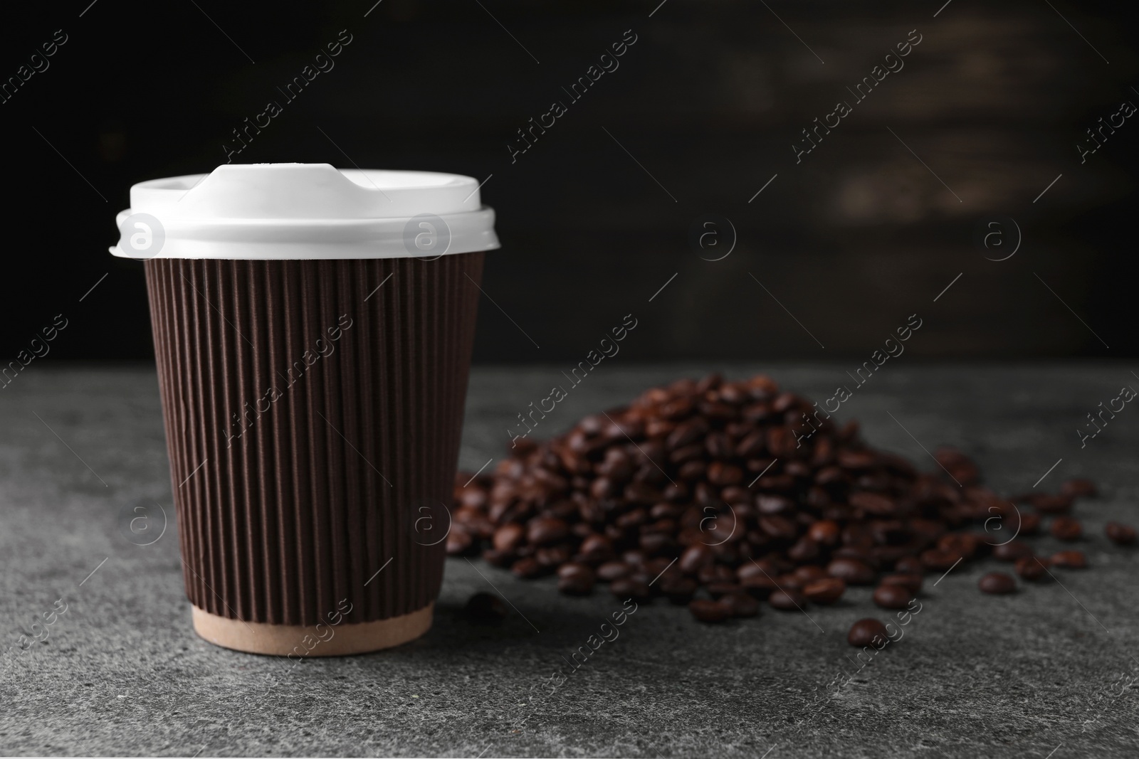 Photo of Coffee to go. Paper cup and roasted beans on grey table, closeup. Space for text