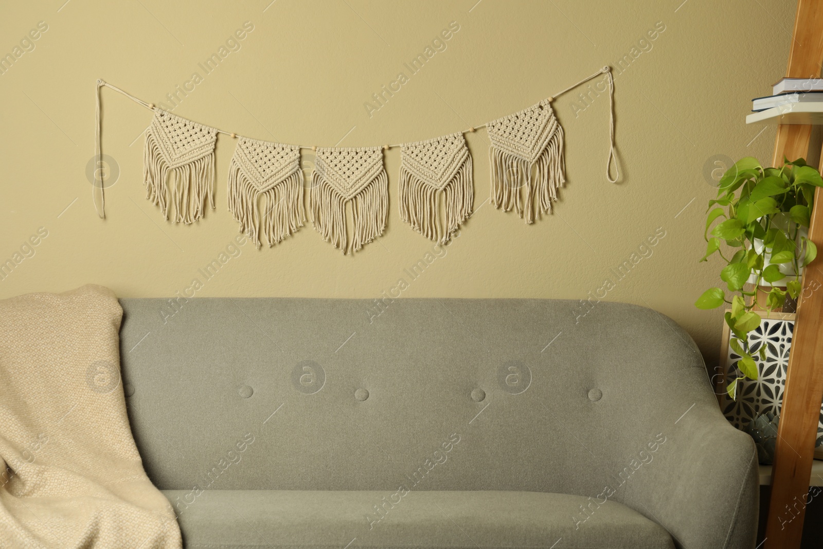 Photo of Beautiful large macrame hanging on beige wall in living room. Decorative element