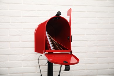 Open red letter box with envelopes near white brick wall