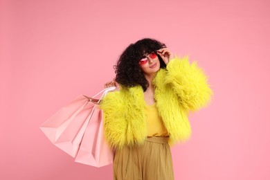 Happy young woman with shopping bags on pink background