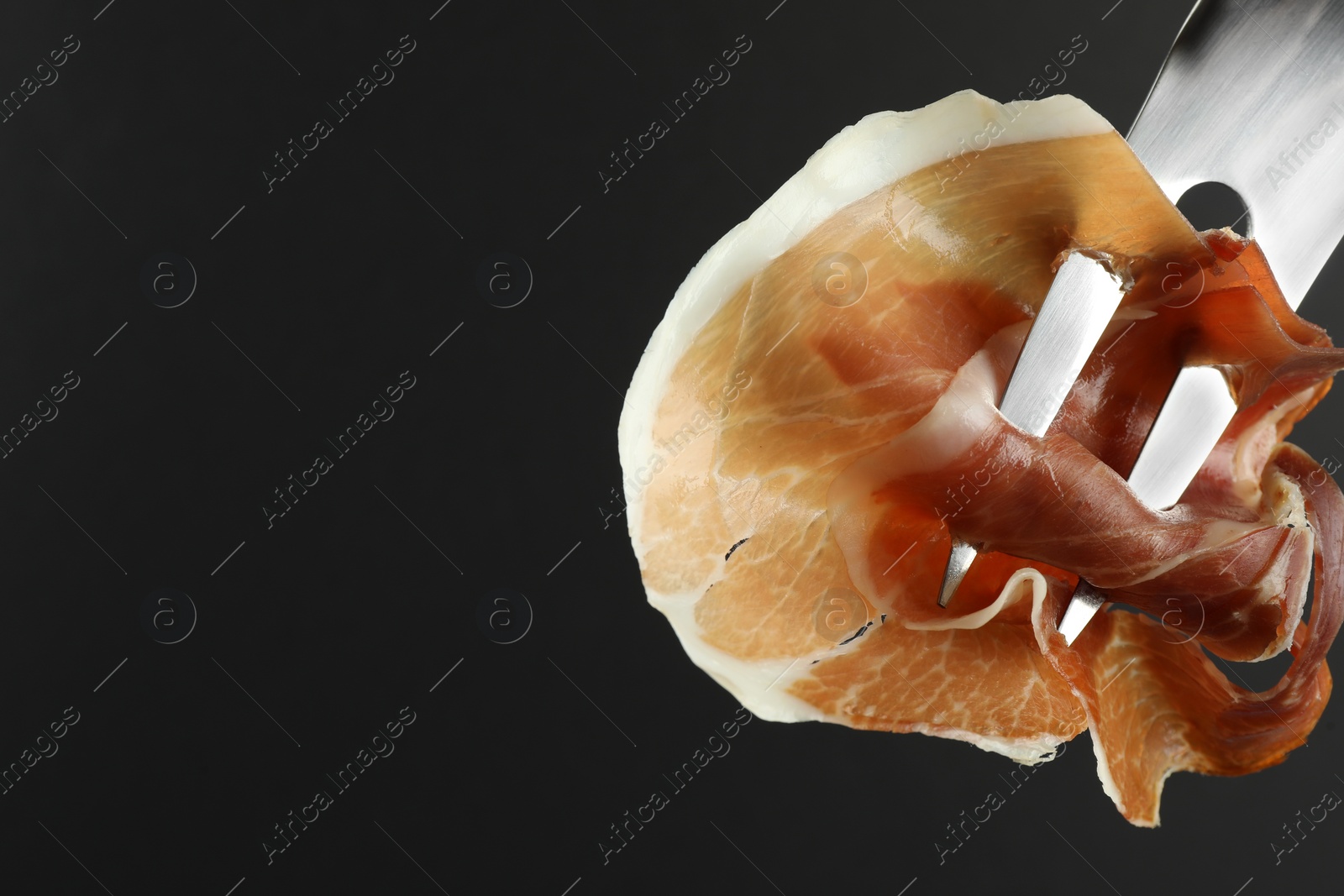 Photo of Fork with slice of tasty jamon on black background, closeup. Space for text