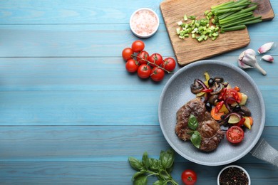 Photo of Tasty fried steak with vegetables in pan and ingredients on light blue wooden table, flat lay. Space for text