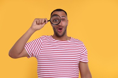 Photo of Excited man looking through magnifier glass on orange background