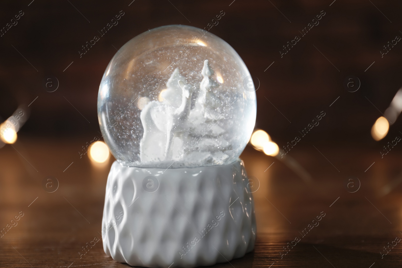 Photo of Snow globe with Christmas lights on wooden table, closeup