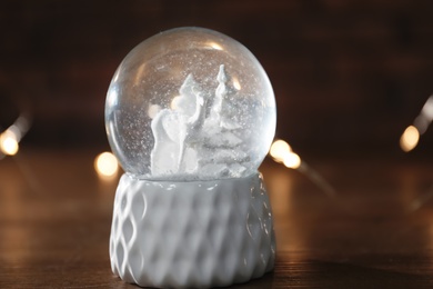 Snow globe with Christmas lights on wooden table, closeup