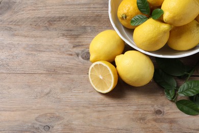 Fresh lemons and green leaves on wooden table. Space for text