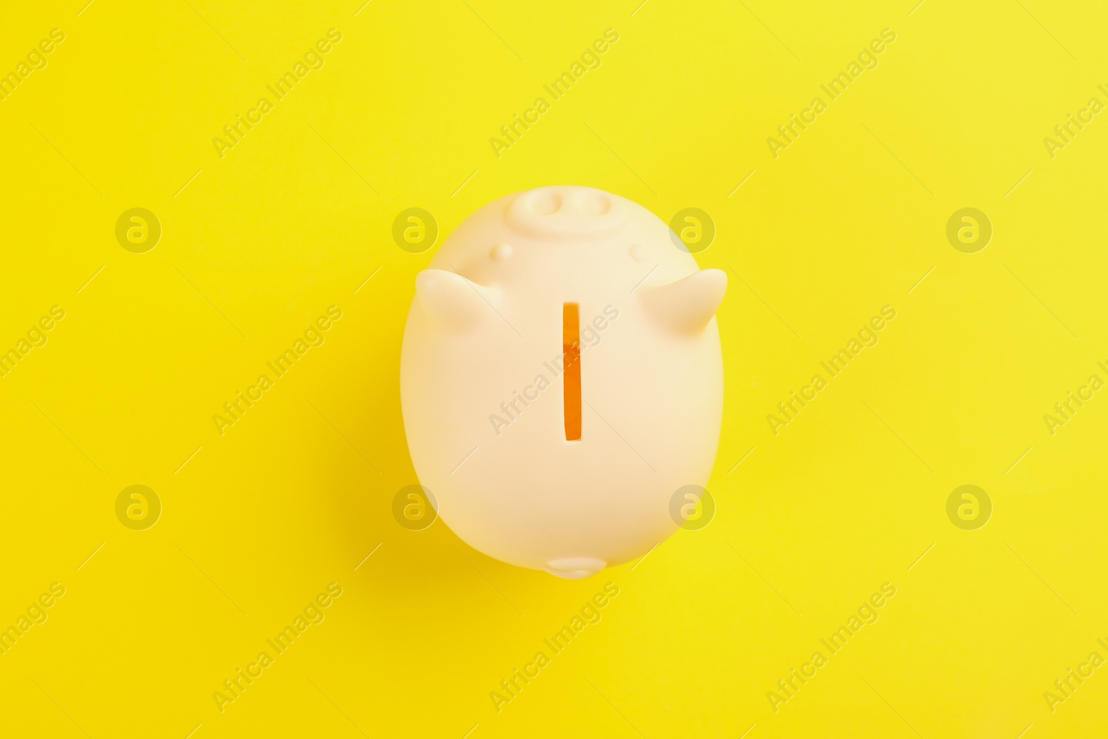 Photo of Beige piggy bank on yellow background, top view