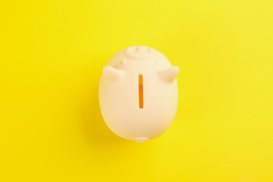 Photo of Beige piggy bank on yellow background, top view