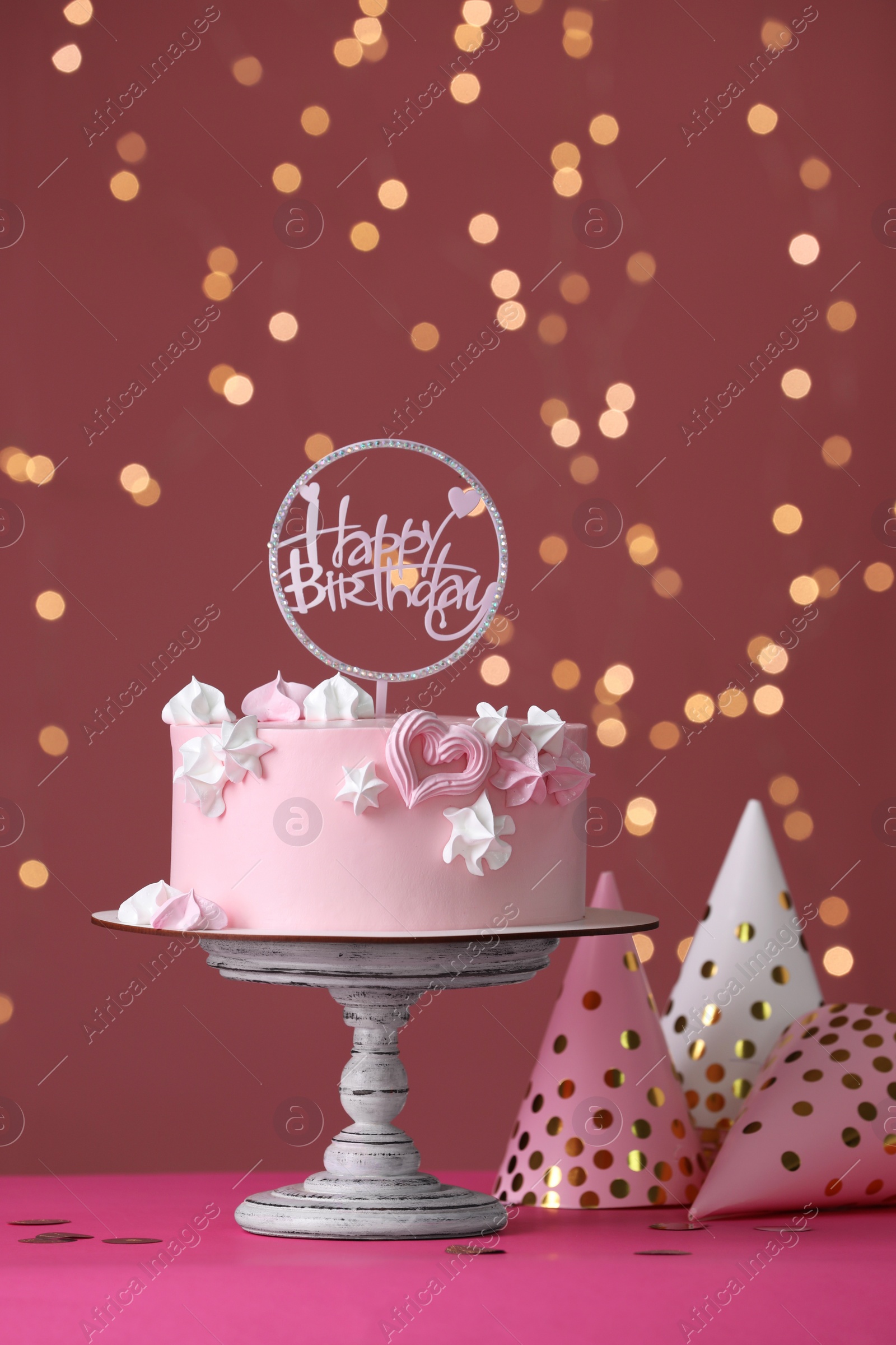 Photo of Beautifully decorated birthday cake on pink table against blurred festive lights