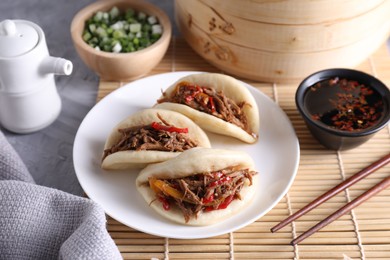 Photo of Delicious gua bao (pork belly buns), chopsticks, green onion and sauce on grey textured table, closeup