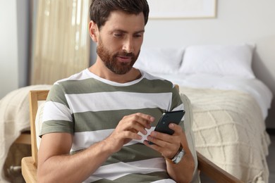 Photo of Handsome man using smartphone in armchair at home