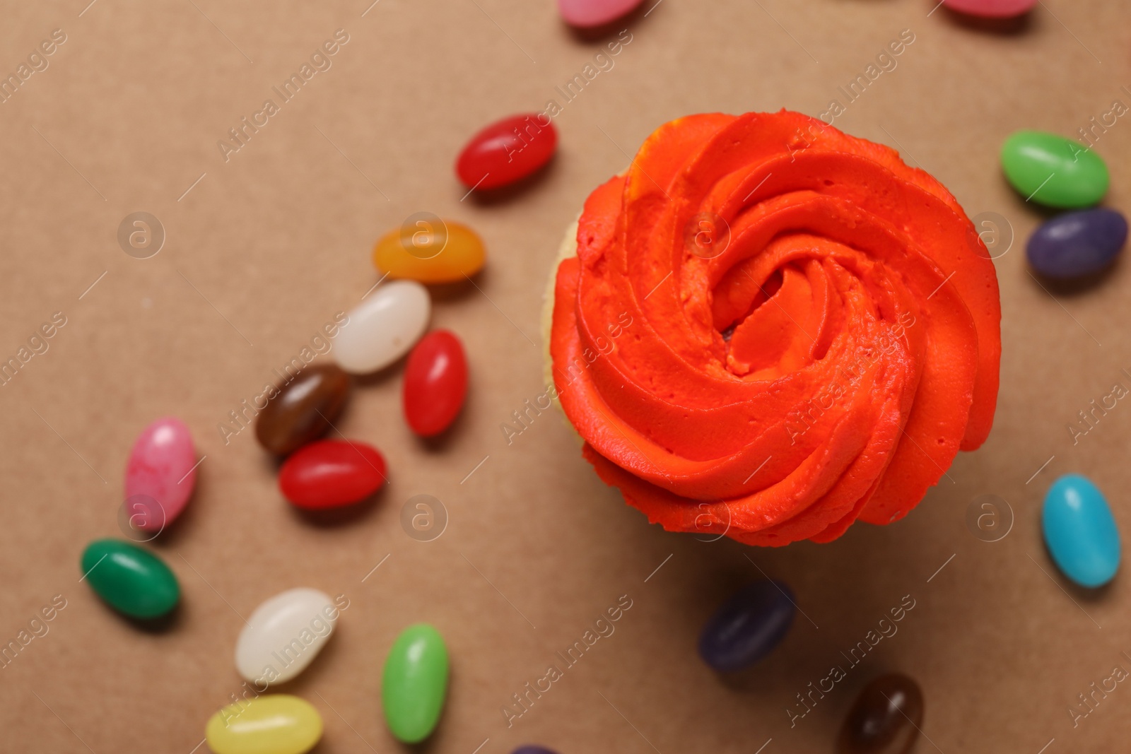 Photo of Delicious cupcakes with bright cream and candies on brown background, flat lay