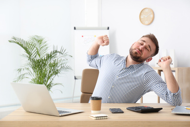 Photo of Lazy young office employee stretching at workplace