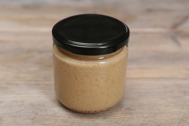 Photo of Tasty nut paste in jar on wooden table, closeup