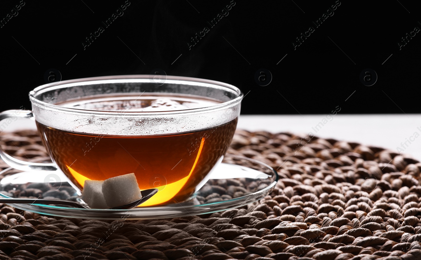 Photo of Glass cup of tea with sugar cubes on table against black background, closeup. Space for text