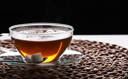 Photo of Glass cuptea with sugar cubes on table against black background, closeup. Space for text