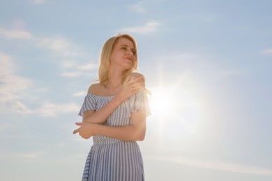 Beautiful young woman against blue sky on sunny day, space for text