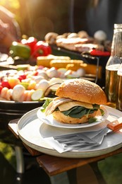 Photo of Tasty burger on table near barbecue grill outdoors