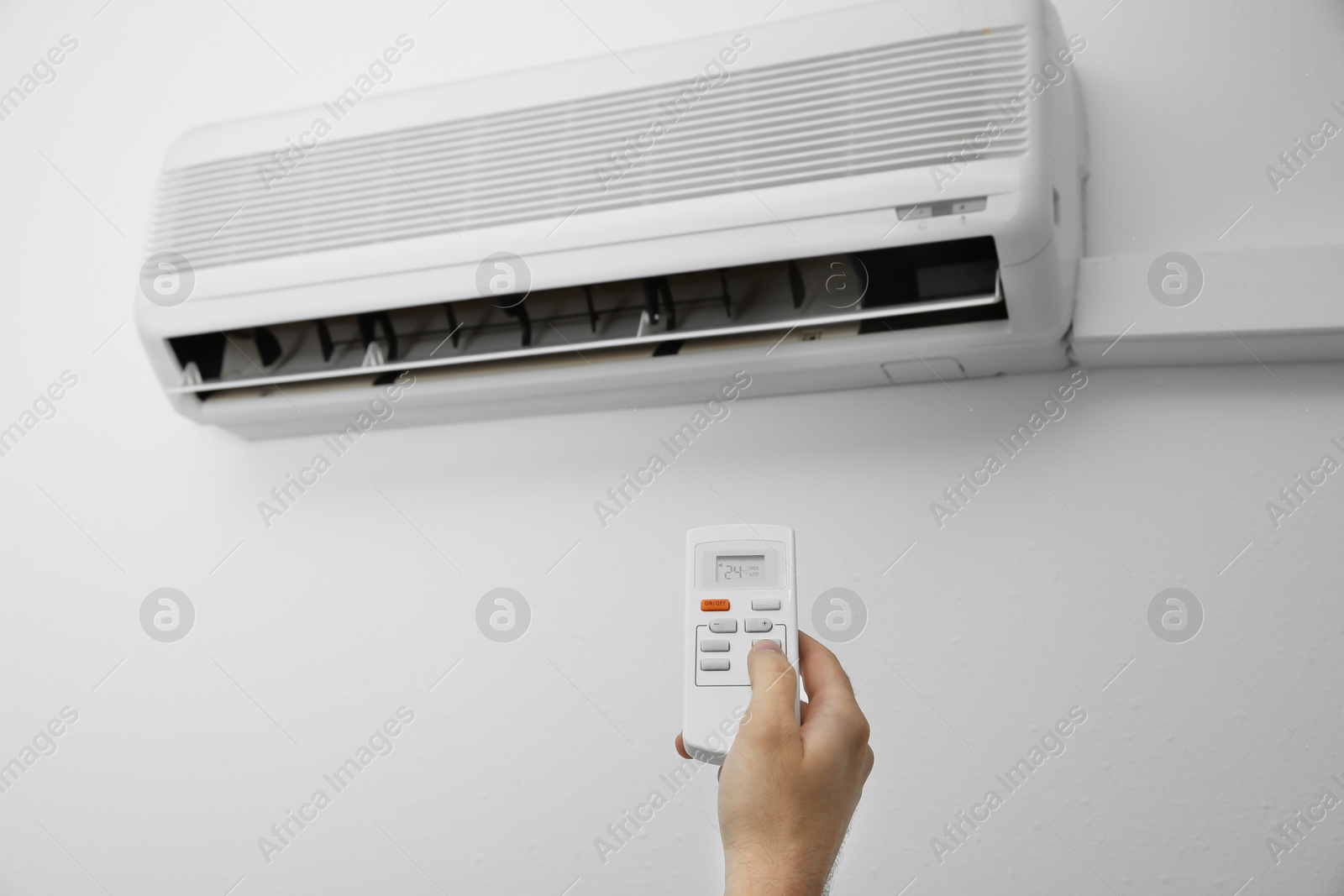 Photo of Man operating air conditioner with remote control indoors