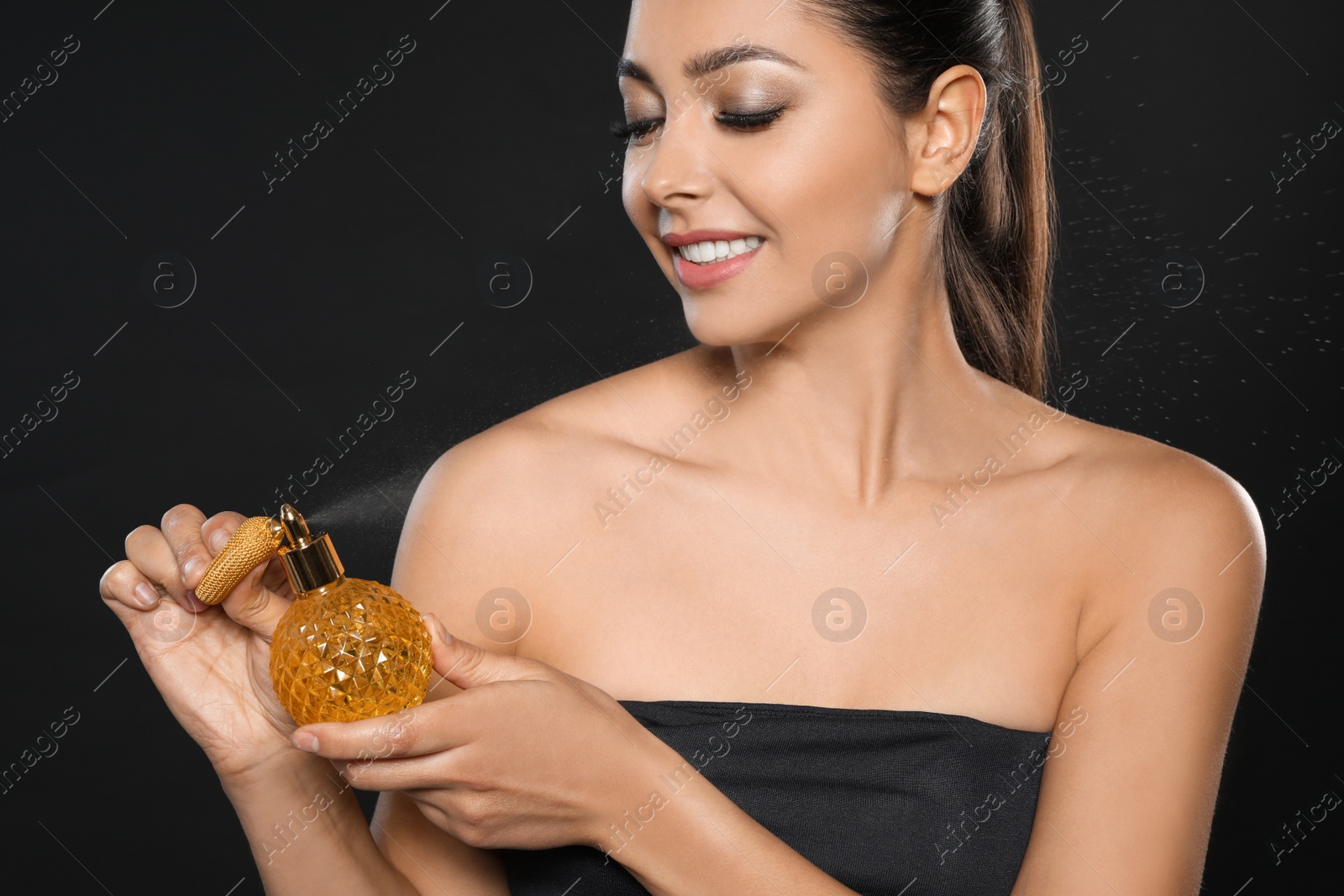 Photo of Young woman spraying perfume on black background