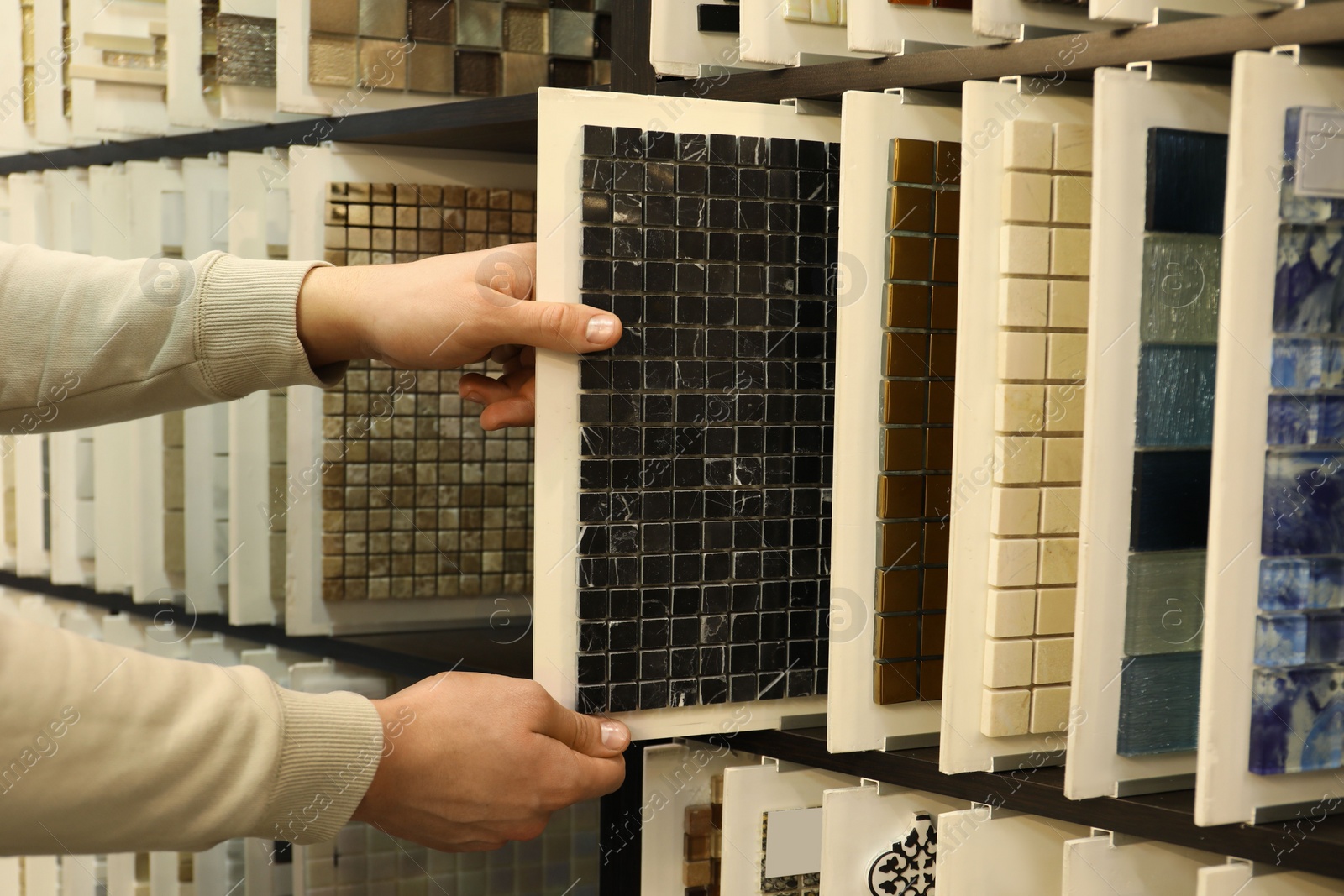 Photo of Man choosing tile among different samples in store, closeup