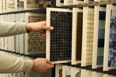 Photo of Man choosing tile among different samples in store, closeup