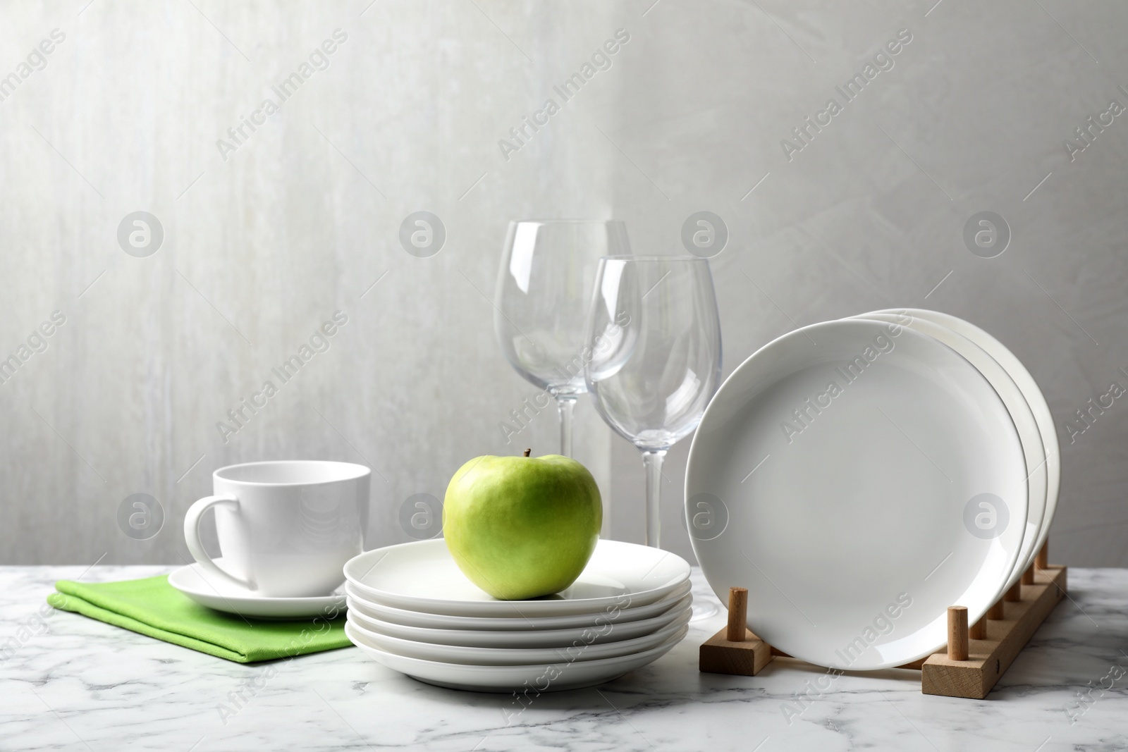 Photo of Set of clean dishware, glasses and apple on white marble table