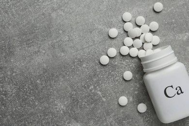 Photo of Overturned bottle of calcium supplement pills on grey table, flat lay. Space for text