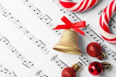 Golden shiny bell with red bow, candy canes and Christmas baubles on music sheets, flat lay and space for text