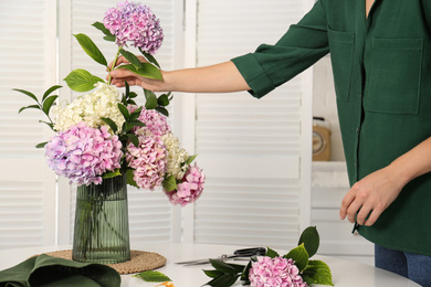 Woman making bouquet with beautiful hydrangea flowers at table indoors, closeup. Interior design element