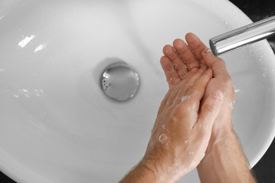 Photo of Man washing hands with soap over sink in bathroom, top view. Space for text