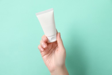 Photo of Woman with tube of hand cream on turquoise background, closeup