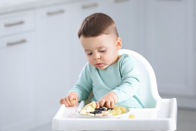 Photo of Cute little baby eating healthy food in high chair at home