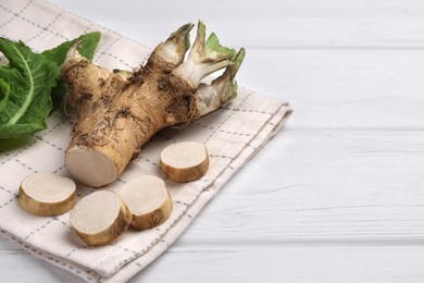 Photo of Cut horseradish root and leaves on white wooden table, closeup. Space for text