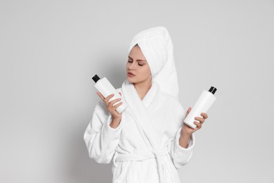 Photo of Beautiful young woman in bathrobe holding bottles of shampoo on light grey background