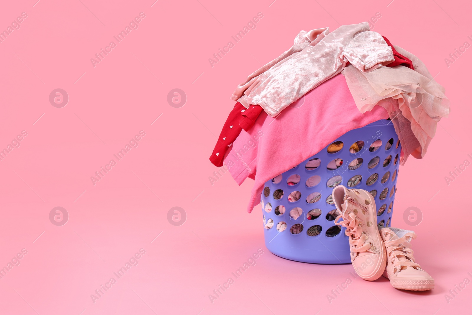 Photo of Laundry basket with baby clothes near shoes on light pink background. Space for text