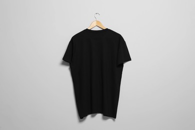 Photo of Hanger with black t-shirt on light wall. Mockup for design