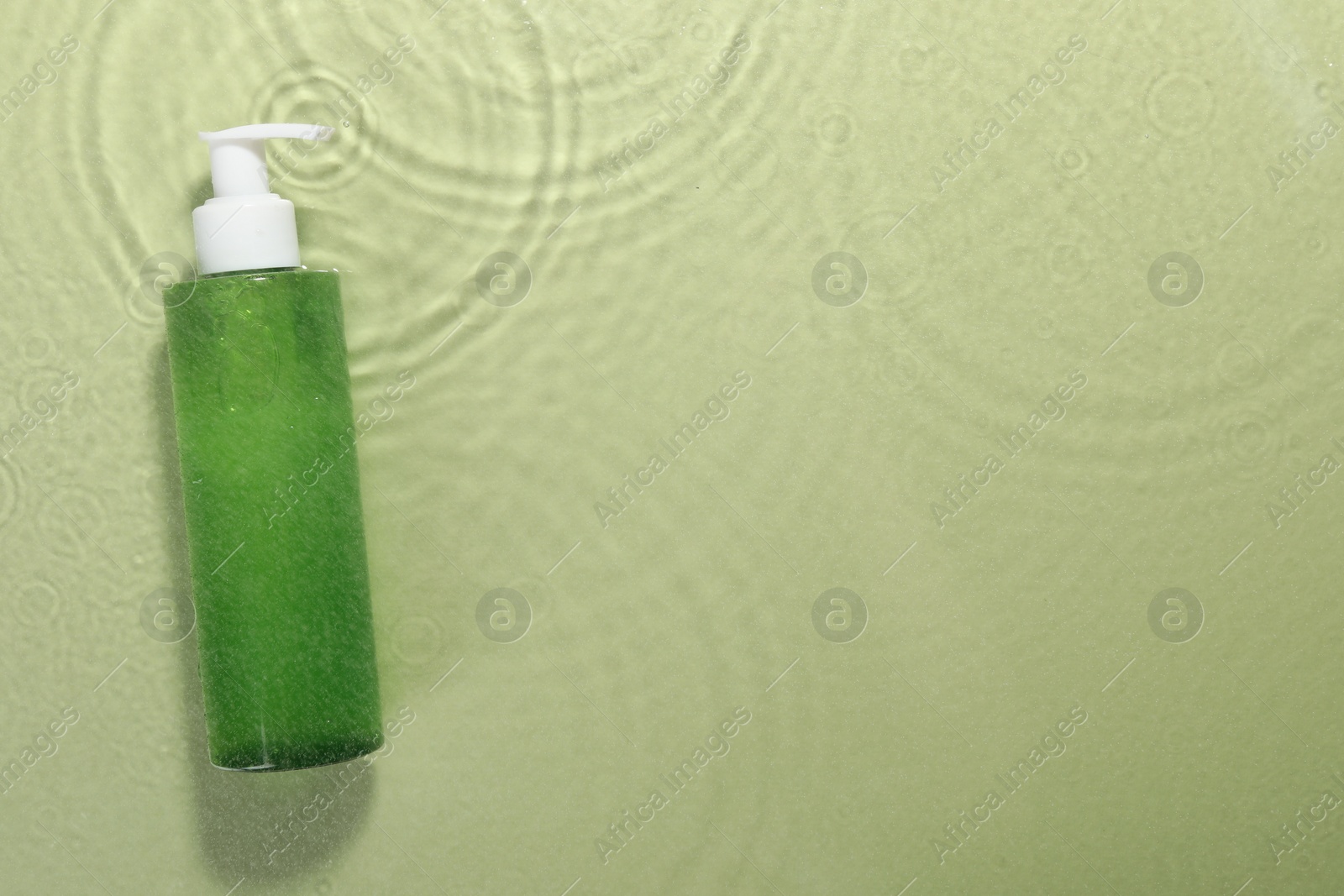Photo of Bottle of facial cleanser in water against olive background, top view. Space for text