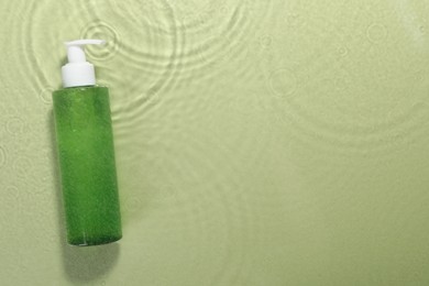 Photo of Bottle of facial cleanser in water against olive background, top view. Space for text