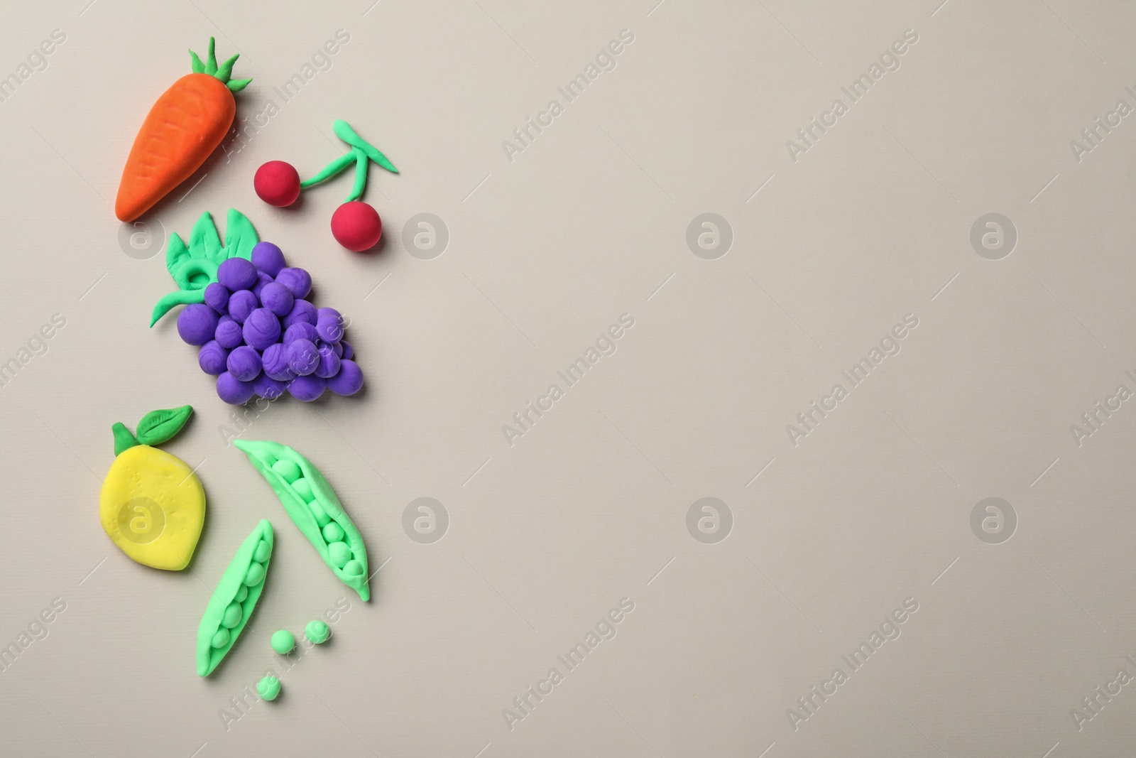 Photo of Different fruits and vegetables made from play dough on light grey background, flat lay. Space for text