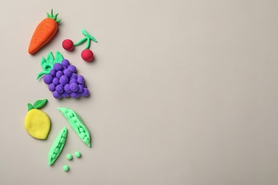 Photo of Different fruits and vegetables made from play dough on light grey background, flat lay. Space for text