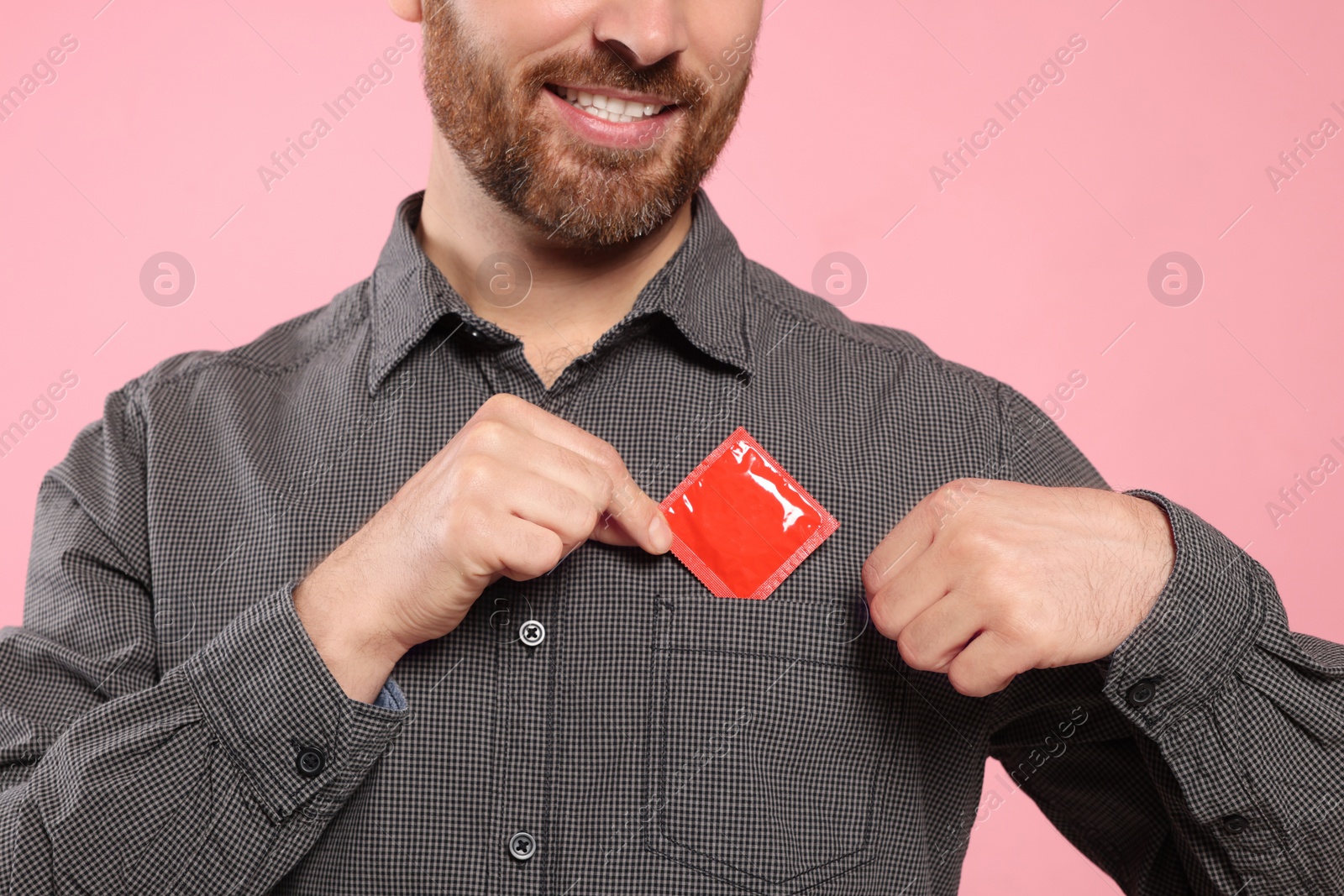 Photo of Man putting condom in his pocket on pink background, closeup. Safe sex