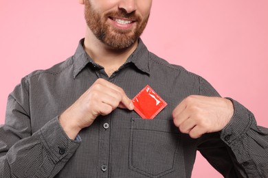 Man putting condom in his pocket on pink background, closeup. Safe sex